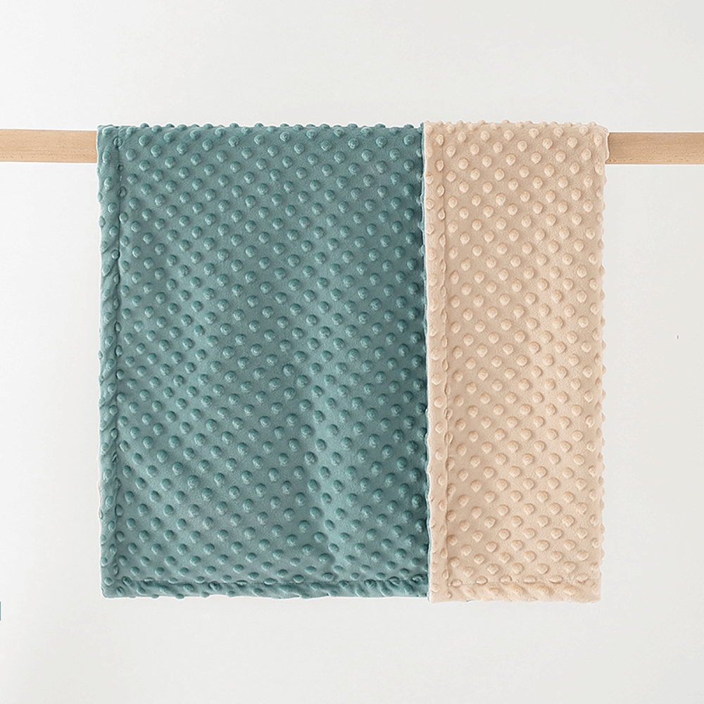 Ultra soft dotted baby blanket in teal and beige hanging on a rail.